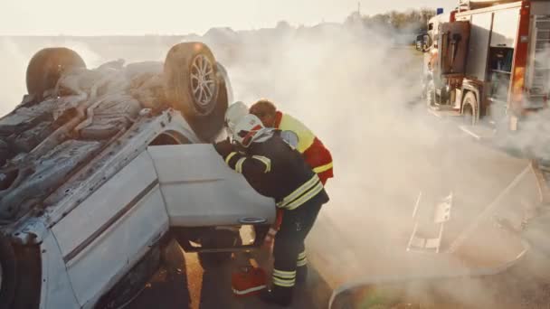 Op de auto crash verkeersongeval scene: Rescue team van brandweerlieden Trek vrouwelijk slachtoffer uit rollover voertuig, ze gebruiken brancards, overhandigen haar aan paramedici die eerste hulp doen. Hoge hoek — Stockvideo