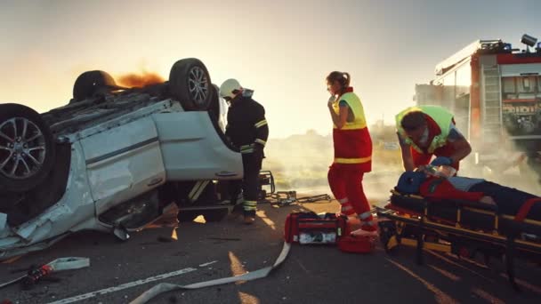 O dopravní nehodě při autonehodě: Záchranáři a hasiči Zachraňte zraněné oběti v pasti. Doktoři dávají první pomoc ženám na nosítkách. Hasiči použít hydraulické řezačky rozmetadlo k otevření vozidla — Stock video