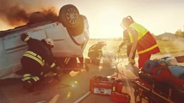 交通事故で:救急車や消防士は負傷者を救出トラップ。医学はストレッチャーの女性への最初の援助を与えます.消防士は、オープン車両に普及油圧カッターを使用しています — ストック動画