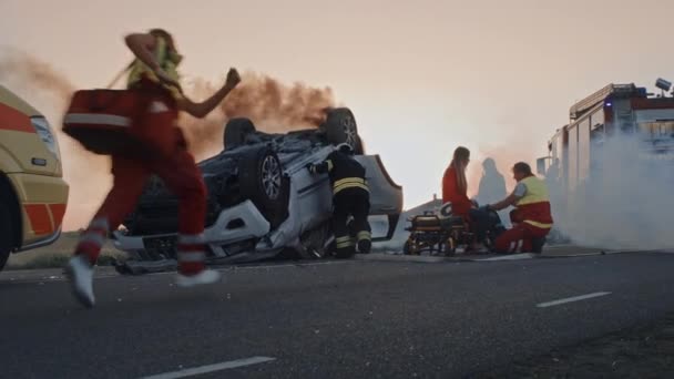 Accidente de tráfico: paramédicos y bomberos rescatan a víctimas heridas atrapadas. Los médicos dan primeros auxilios a una pasajera. Los bomberos utilizan separador de cortadores hidráulicos para abrir el vehículo — Vídeos de Stock