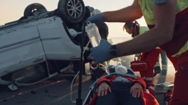 Araba kazasında trafik kaza sahnesinde: sağlık görevlileri sedye üzerinde yatan bir yolcu yaşam kaydedin. Kurtarma Itfaiyeciler diğer araç hapsedilmiş kurbanlar almak için rollover araç girin