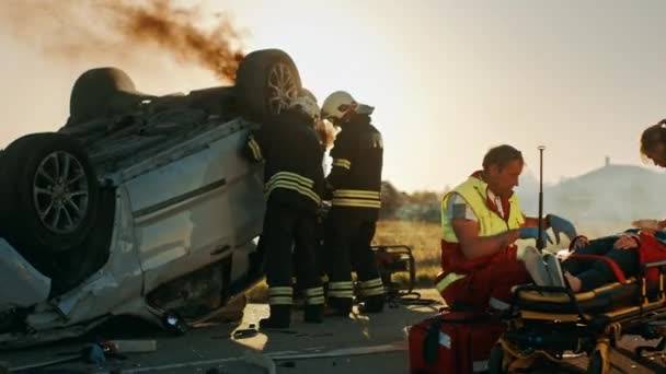 En la escena del accidente de tráfico: Los paramédicos salvan la vida de un pasajero acostado en camillas. Escuchan un latido del corazón, utilizan la máscara de oxígeno, configuración Drop Counter. Bomberos utilizan cortadores para abrir el coche — Vídeo de stock