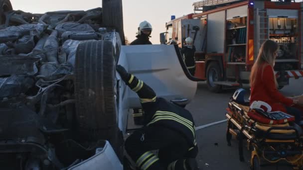 Autóbaleset: mentősök és tűzoltók mentik meg a csapdába esett áldozatokat. A mentősök elsősegélyt adnak egy női utasnak. Tűzoltók használja hidraulikus vágó szóró nyitott jármű — Stock videók