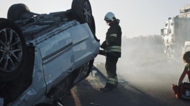 Araba kazasında trafik kaza sahnesinde: sağlık görevlisi kaza kadın kurbanı Ilk yardım oksijen maskesi veren. İtfaiyeciler ateşi söndürüp diğer yolcuları serbest bırakmak için Hidrolik kesici kullanın