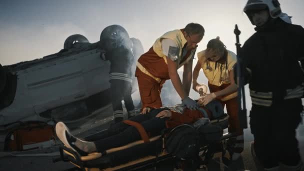 На сцене ДТП: Парамедики спасают жизнь женщине-жертве, которая лежит на носилках. Они применяют кислородную маску, проводят сердечно-легочную реанимацию и первую помощь — стоковое видео