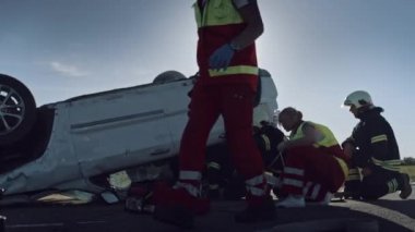 Araba kazasında trafik kaza sahnesinde: sağlık görevlisi kaza kadın kurbanı Ilk yardım oksijen maskesi veren. İtfaiyeciler ateşi söndürüp diğer yolcuları serbest bırakmak için Hidrolik kesici kullanın