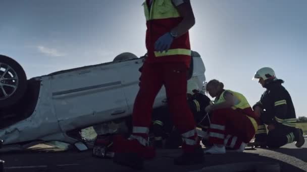 Na místě nehody při autonehodě: Paramedics poskytující první pomoc kyslíkovou masku obětem nehody. Hasiči uhasit oheň a použít hydraulický střihač pro volné ostatní pasažéry — Stock video