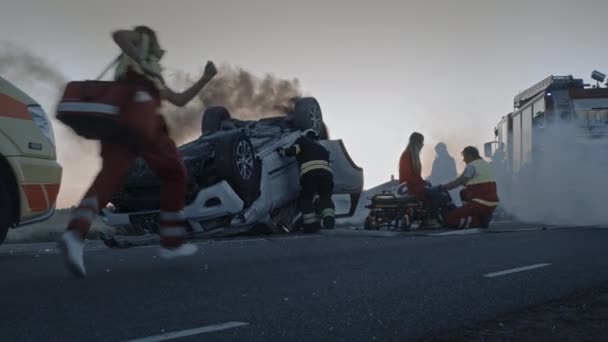 Incidente stradale d'incidente d'auto: paramedici e vigili del fuoco soccorsi feriti vittime intrappolate. I medici danno il primo soccorso a una barella passeggera scioccata. I pompieri usano tagliatori idraulici per aprire il veicolo — Video Stock