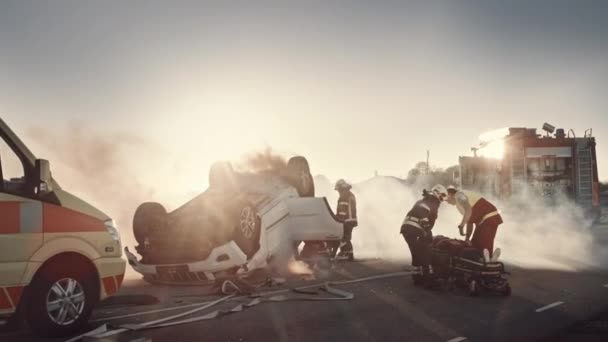 On the Car Crash Traffic Accident Scene: Rescue Team of Firefighters Trek Vrouwelijke Slachtoffer uit Rollover Vehicle, Ze gebruiken Stretchers zorgvuldig, Geef haar over aan paramedici die EHBO uitvoeren — Stockvideo