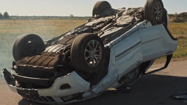 Incidente stradale terribile Rollover Fumare e bruciare veicolo sdraiato sul tetto in mezzo alla strada dopo la collisione. Scena di crash diurno con auto danneggiata — Video Stock