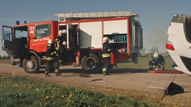 Пожарные прибывают на место аварии на пожарной машине. Пожарные хватают свои инструменты, снаряжение и снаряжение из пожарной машины, спешат на помощь раненым, попавшим в ловушку людям. Slow Motion — стоковое видео