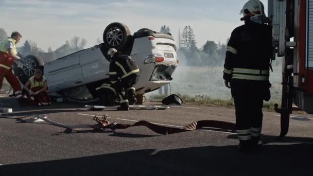 Equipe de resgate de bombeiros e paramédicos Trabalhar em uma cena terrível acidente de carro. Preparando equipamentos, alongamentos, primeiros socorros. Salvando pessoas feridas e presas do veículo em chamas — Vídeo de Stock