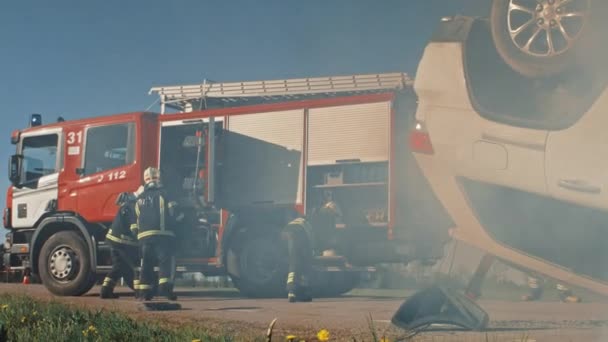 Спасательная команда пожарных прибывает в аварию, катастрофу, пожарную часть на своей пожарной машине. Пожарные хватают снаряжение, готовят пожарные шланги и шестерни из пожарной машины, спешат на помощь раненым. — стоковое видео