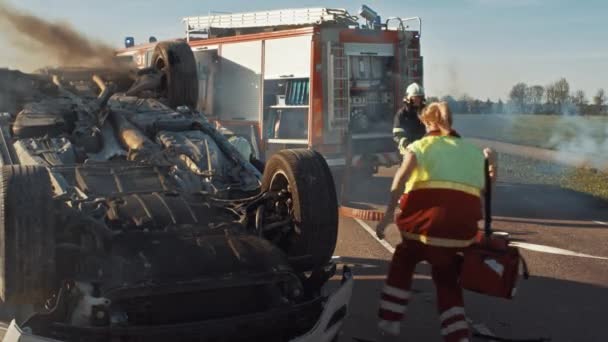 Equipo de rescate de bomberos y paramédicos trabajan en una terrible escena de accidente de tráfico. Preparación de equipos, estiramientos, primeros auxilios. Salvar a las personas heridas y atrapadas del vehículo en llamas — Vídeo de stock