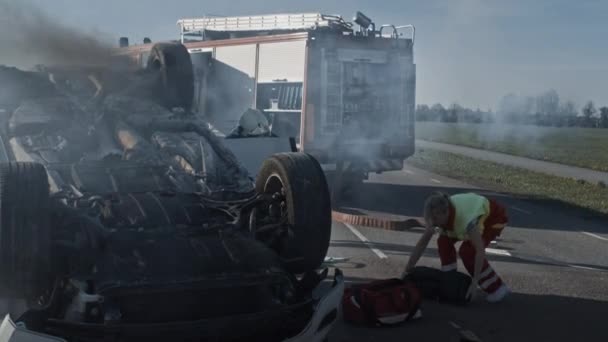 Equipo de rescate de bomberos y paramédicos trabajan en una terrible escena de accidente de tráfico. Preparación de equipos, estiramientos, primeros auxilios. Salvar a las personas heridas y atrapadas del vehículo en llamas — Vídeo de stock