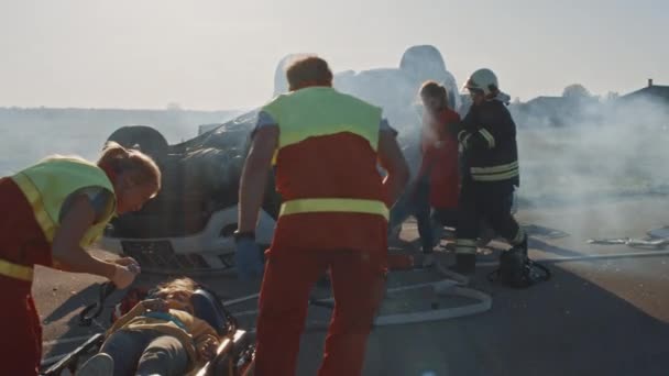 Op de auto crash verkeersongeval scene: paramedics redden van het leven van een klein meisje liggend op brancards, ze krijgt eerste hulp hulp. Brandweerlieden gratis andere passagiers gevangen in rollover voertuig — Stockvideo