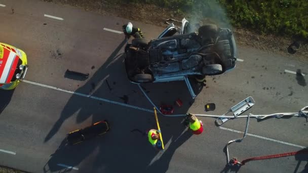 Aerial view: Rescue team van brandweerlieden en paramedici werken aan een auto crash verkeersongeval scene. Het voorbereiden van apparatuur, EHBO hulp. Het redden van gewonden en gevangen mensen uit het voertuig. Uitzoomen — Stockvideo