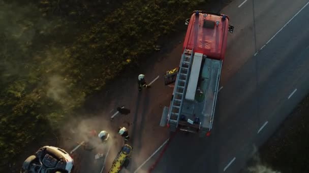 Luftaufnahme: Rettungsteam aus Feuerwehrleuten und Rettungssanitätern bei der Arbeit an der Unfallstelle. Ausrüstung vorbereiten, Erste Hilfe leisten. Rettung verletzter und eingeklemmter Personen aus brennendem Fahrzeug — Stockvideo