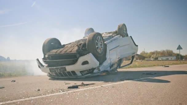 Τρομακτικό τροχαίο ατύχημα, Rollover Κάπνισμα και κάψιμο του οχήματος που βρίσκεται στην οροφή του στη μέση του δρόμου μετά τη σύγκρουση. Daytime Crash σκηνή με σοβαρά κατεστραμμένο αυτοκίνητο. — Αρχείο Βίντεο