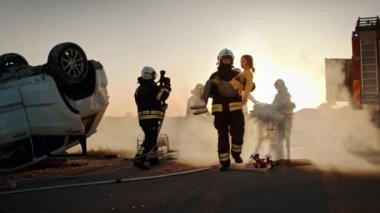 Cesur İtfaiyeci Yaralı Genç Kızı Sevgi dolu annesine kavuştuğu güvenli bir yere taşıyor. Arkaplan Kazasında Trafik Kazasında Cesur Sağlık Görevlileri ve İtfaiyeciler Hayat Kurtarıyor