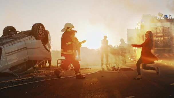 Coraggioso pompiere porta ferito giovane ragazza in salvo dove si riunì con la sua amata madre. Sullo sfondo incidente stradale auto incidente coraggiosi paramedici e vigili del fuoco salvare vite umane — Video Stock