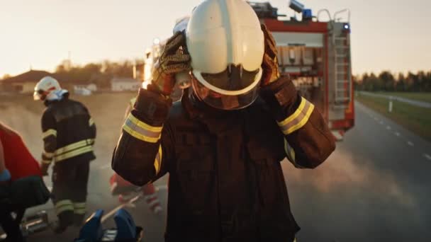 Portret dzielnego strażaka zabierając jego hełm. W tle odważni bohaterowie Paramedics i strażaków Rescue Team Walka ognia, dym i uratować ludzi s mieszka. — Wideo stockowe