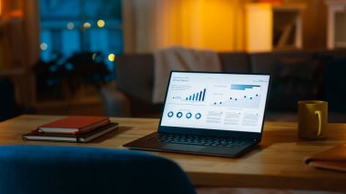 Istatistik Infographics gösteren dizüstü bilgisayar oturma odasında bir masada duruyor. Arka planda sıcak ışıklar ile rahat oturma odası.