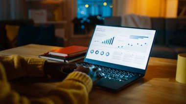 Istatistik Infographics gösteren dizüstü bilgisayar oturma odasında bir masada duruyor. Arka planda sıcak ışıklar ile rahat oturma odası.