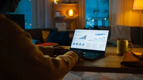 Over the Shoulder Shot : Woman Sitting at Her Desk travaille sur un ordinateur portable qui montre des statistiques et des infographies. tard la nuit dans son salon femme utilise ordinateur . — Photo