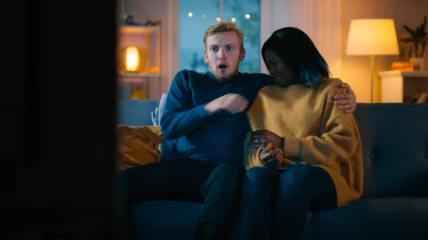 Happy Young Couple Watching Horror Movie on TV while Sitting on a Couch, they got Scared, Girl Covers eyes. Handsome Caucasian Boy and Black Girl in Love Spending Time Together. — Stock Photo, Image