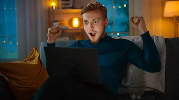 In the Evening: Portrait of Handsome Young Man Using Laptop while Sitting on a Couch at Home, Suddenly He Wins Big and Celebrates His Victory with YES Gesture. — Stock Photo, Image