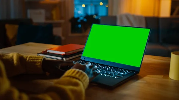 Mooie zwarte vrouw zittend op haar bureau werkt op een laptop met groen mock-up scherm. Laat in de nacht in haar woonkamer meisje maakt gebruik van notebook computer. — Stockfoto