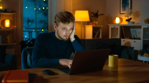Υπνηλία και εξαντλημένος άνθρωπος δουλεύει σε ένα φορητό υπολογιστή ενώ κάθεται στο γραφείο του στο σπίτι στη μέση της νύχτας. — Φωτογραφία Αρχείου