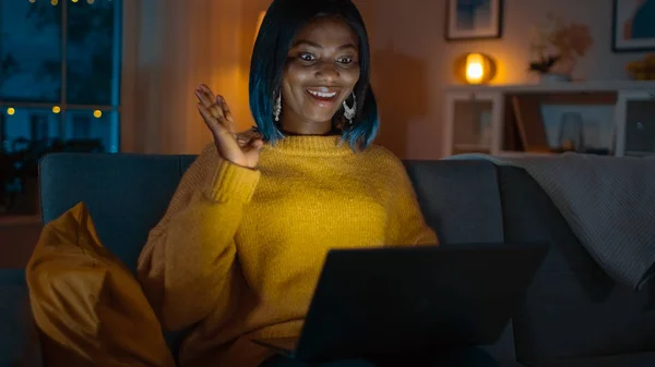 Πορτραίτο του όμορφη χαμογελαστή μαύρο κορίτσι στο σπίτι, καθισμένος σε έναν καναπέ χρησιμοποιώντας φορητό υπολογιστή για να κάνετε μια κλήση βίντεο, λέει Γεια. Στο βράδυ κορίτσια συνομιλίες με συγγενείς και φίλους χρησιμοποιώντας υπολογιστή κάμερα. — Φωτογραφία Αρχείου