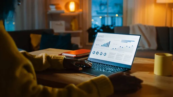 Laptop-Computer mit statistischen Infografiken steht auf einem Schreibtisch im Wohnzimmer. im Hintergrund gemütliches Wohnzimmer mit warmem Licht. — Stockfoto