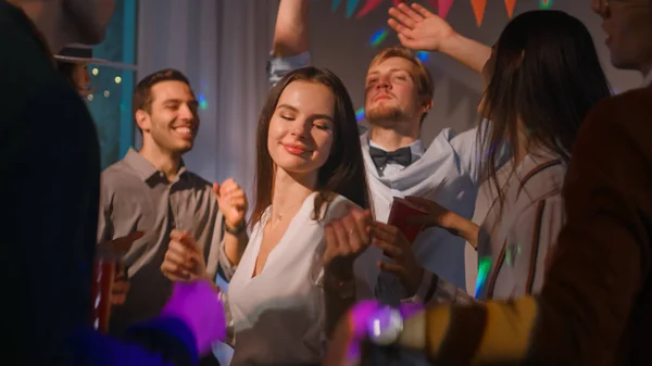 Bei der Hausparty: eine bunte Gruppe von Freunden hat Spaß, tanzt, springt, trifft sich und trinkt. Stilvolle junge Leute beim Clubbing. Disco-Neonlichter. — Stockfoto