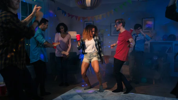 Op het College House Party: sexy paar dansen met een gevarieerde groep vrienden die plezier om hen heen. Jongens en meisjes clubbing in de woonkamer. Disco Neon strobe verlichting verlicht kamer. — Stockfoto