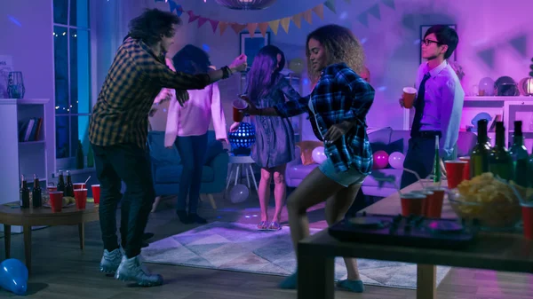 Bei der College-House-Party: Eine bunte Gruppe von Freunden hat Spaß, tanzt und trifft sich. Jungen und Mädchen tanzen im Kreis. Disco-Neonlicht erhellt Raum. — Stockfoto