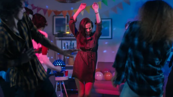 Auf der College House Party: junges Mädchen tanzt inmitten eines Personenkreises. Eine bunte Gruppe von Freunden hat Spaß, tanzt und trifft sich. Disco-Neonlicht erhellt Raum. — Stockfoto