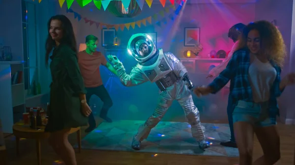 Bei der Kostümparty im College House: Ein lustiger Typ im Weltraumanzug tanzt los und macht moderne Bewegungen. mit ihm tanzen schöne Mädchen und Jungen im Neonlicht. — Stockfoto