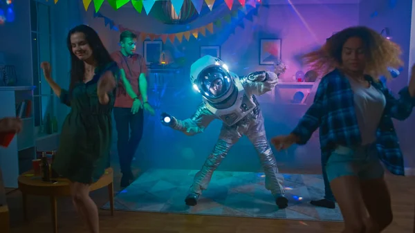 Op de College House kostuum partij: Fun Guy dragen ruimte pak dansen uit, het doen van robot dans moderne moves. Met hem mooie meisjes en jongens dansen in neon lichten. — Stockfoto