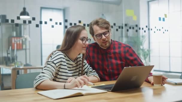 Jonge Casual Business Couple gebruiken Laptop in Creative Agency Loft. Vriendelijke Easygoing Coworking Atmosfeer. Ze bespreken en brainstormen ideeën. Manager legt nieuwe werkstrategie uit. — Stockvideo