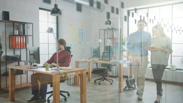 Jonge vrouw en man collega's lopen op kantoor terwijl ze een vriendelijke discussie hebben over nieuwe zakelijke ideeën. Easygoing-Coworking-sfeer in creatief bureau. — Stockvideo