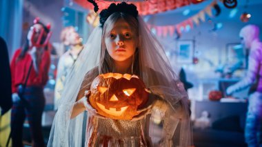 Cadılar Bayramı Kostüm partisi: bir kanlı beyaz gelin elbise tutma yanan kabak kafa küçük kız gülümseyen. Zombi, kan susamış Dracula, Anne, büyülü cadı ve göz kamaştırıcı o şeytan dans