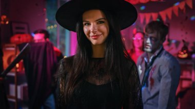 Halloween kostüm partisi: elbise ve şapka giyen muhteşem genç cadı seductively pozlar. Arka plan: güzel o şeytan, korkutucu ölüm, Kont Dracula, dekore edilmiş odada zombi dans