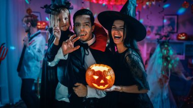 Halloween kostüm partisi: baba Kont Dracula küçük yarasa kız kızı ve mutlu bir aile portre için hugs cadı eşi tutar. Arka plan canavarlar eğlenmek