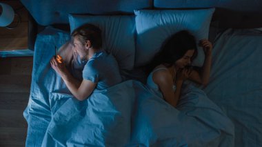 Aldatma ve sadakatsiz genç adam yeni bir tarih bulmak için smarphone kullanır ya da uyuyan gece yatakta kız arkadaşı uyur. Üst görünüm kamera