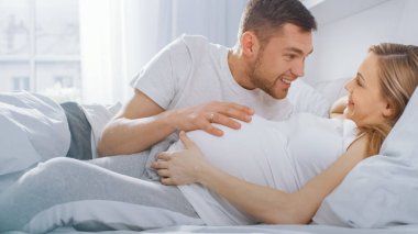 Mutlu genç çift yatakta birlikte cuddling, Genç kadın hamile, sevgi dolu partner eğilir ve bir bebek hareket dinler ve Heartbeat, öpücük Belly. İhale, Aile yaşamı sevgi dolu Moments.
