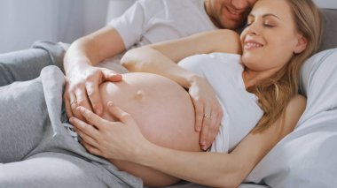Mutlu genç çift yatağa birlikte sarılarak, Genç kadın hamile ve sevgi dolu kocası dokunur ve onun Belly şefkatli caresses. Belly kamera Focus.
