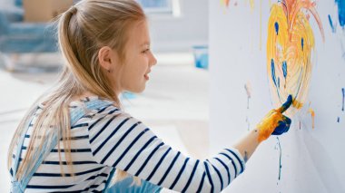 Sarı ve mavi boya daldırılmış eller ile mutlu küçük kız duvar gülümseme ile renkli bir kalp çizer. Eğleniyor ve gülüyor. Ev restore ediliyor.